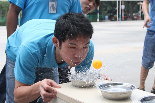 游园活动现场，同学正在玩吹乒乓球游戏